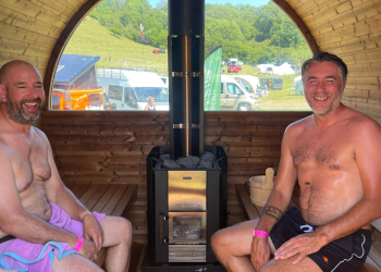 Two men inside sauna next to log burner